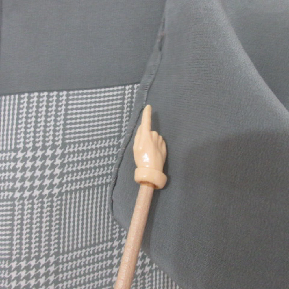Gray fabric with a houndstooth pattern and a wooden stick with a hand-shaped handle.